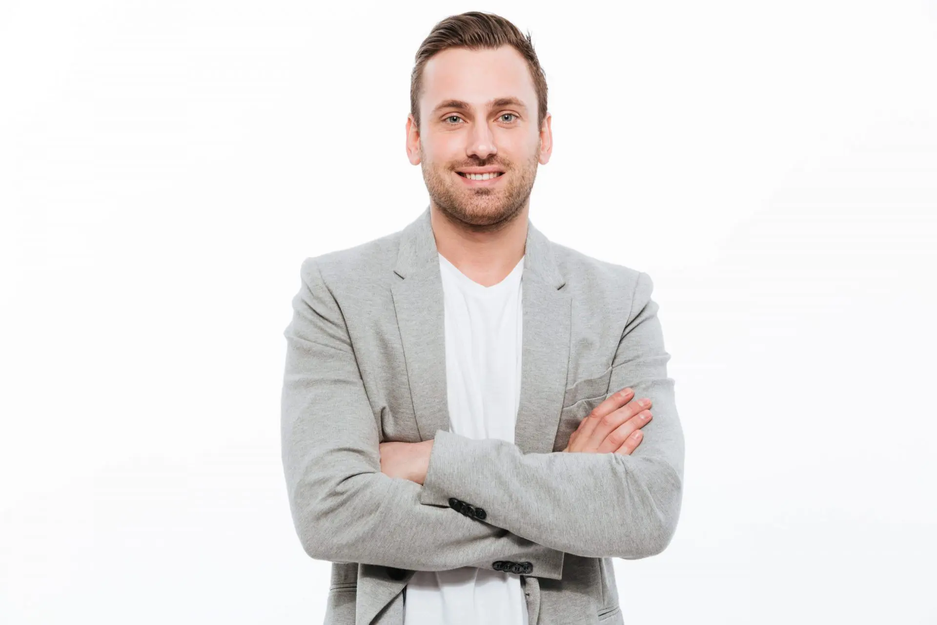 Portrait of successful man having stubble posing on camera with broad smile keeping arms folded isolated over white background